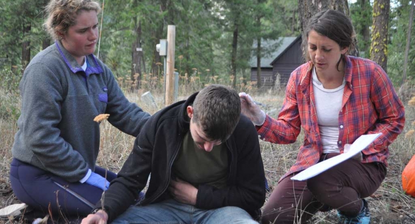 three people participate in a wilderness first responder exercise